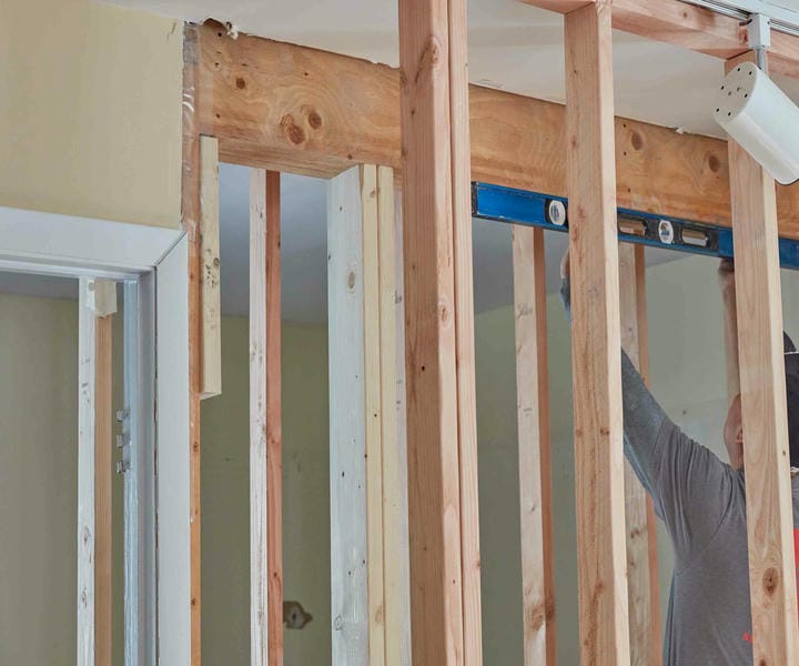 A person is measuring and constructing a wooden wall framework with a level during home renovation work. it seems a wall removal