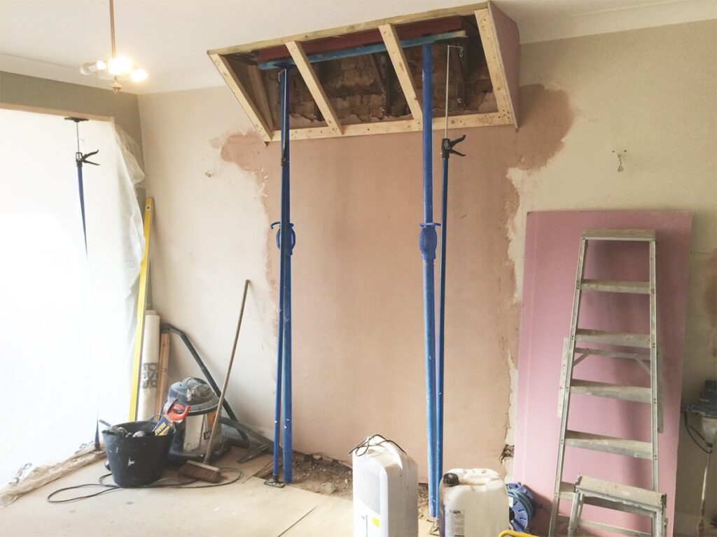 A room under renovation with scaffolding, tools, and part of a wall being removed.