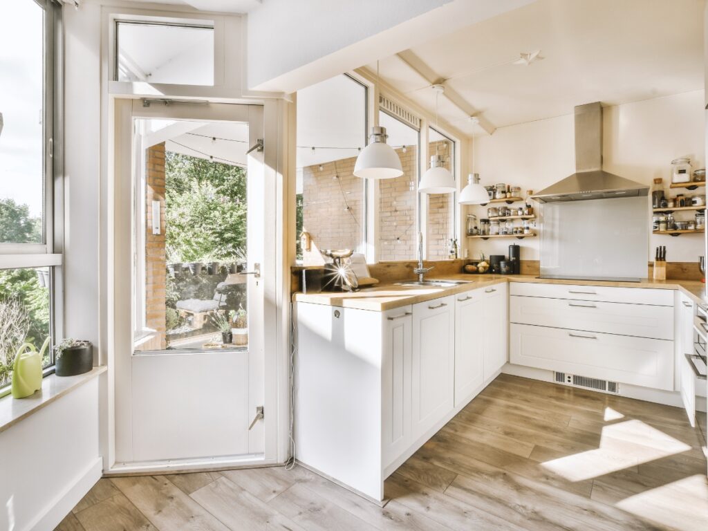 A modern kitchen with white cabinetry, wooden countertops, and large windows.