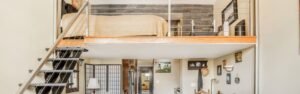Modern loft interior featuring a staircase, upper bedroom area, and stylish decor with a mix of wood and metal elements.
