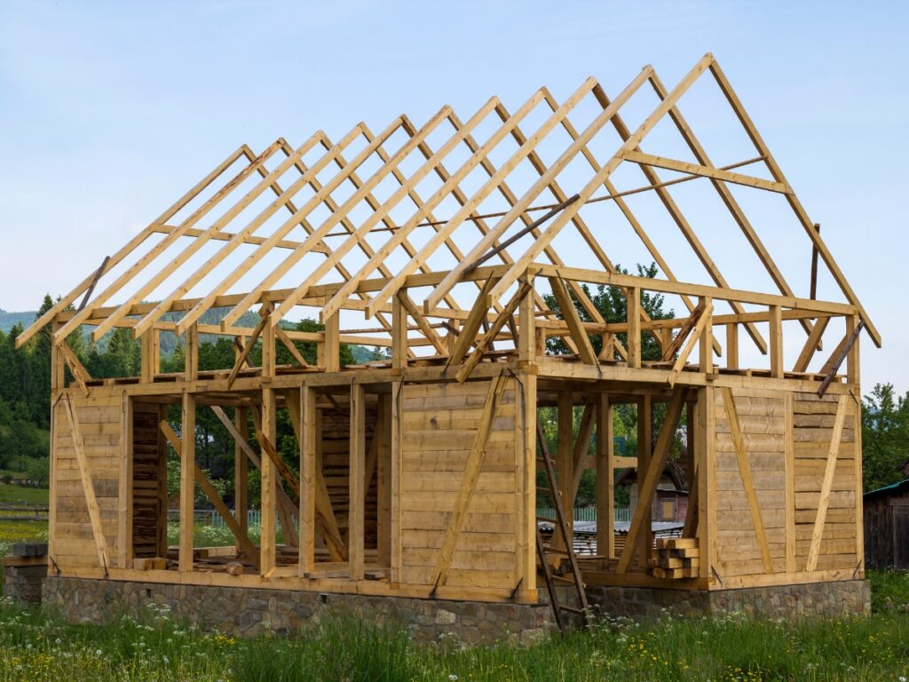 A partially constructed wooden building with a framed structure and roof in an outdoor setting.