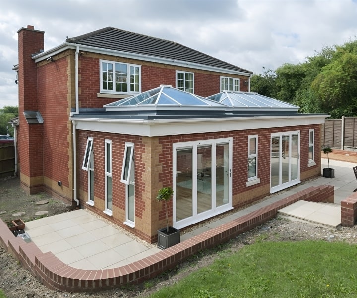 A stylish , two-story brick house with a spacious, glass-enclosed lantern conservatory, surrounded by lawn and patio area.