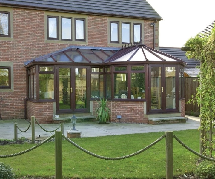 Modish brick house features a large, wooden-framed conservatory with glass panes and a gently sloped roof, surrounded by a green lawn.