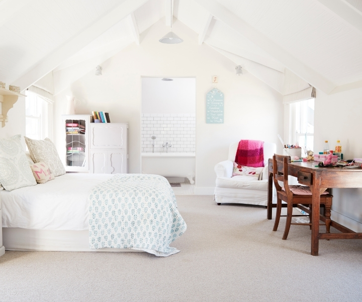 Bright attic bedroom with bed, desk, armchair, and bathroom.