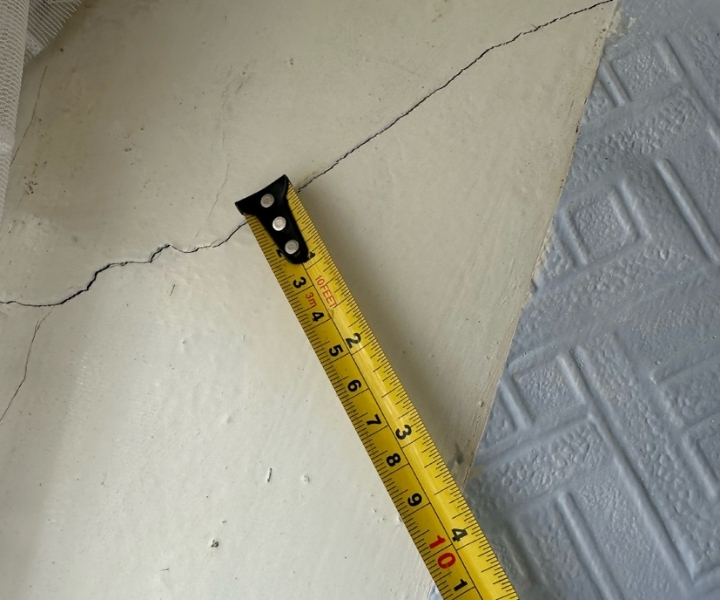 Horizontal crack on wall measured with yellow tape measure.