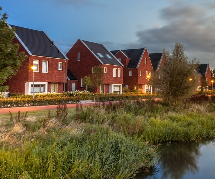 Row of modern red-brick houses beside water at dusk.