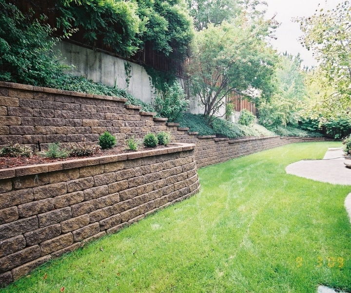 Tiered stone retaining walls with greenery alongside a grassy lawn.