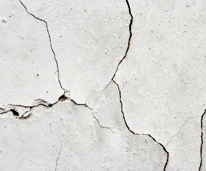 Multiple deep cracks on damaged white plaster wall surface.