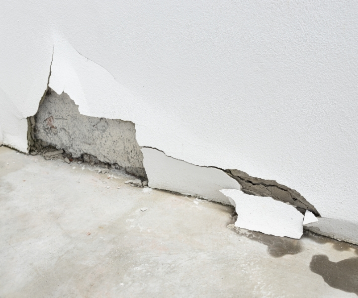 Large crack and damaged plaster on interior wall base.