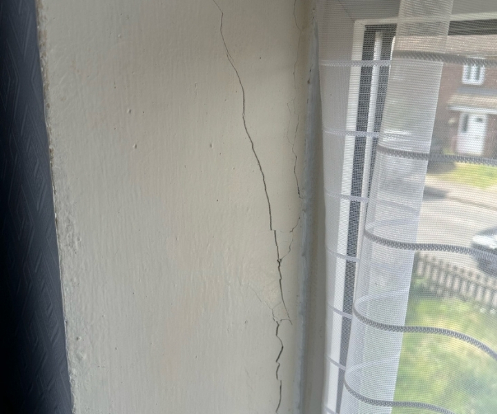 Vertical crack along interior wall beside window frame.