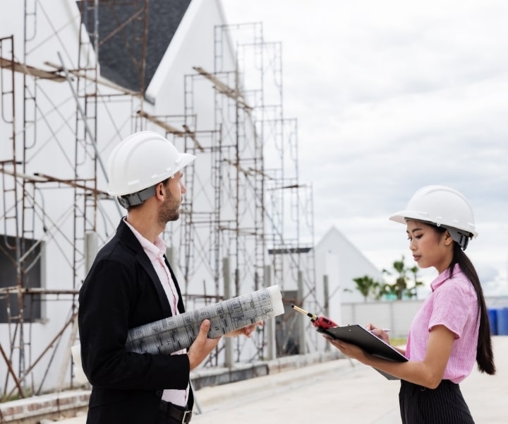 Engineers reviewing construction plans at building site, wearing helmets.