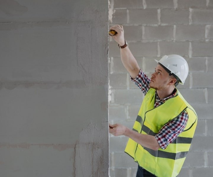 Engineer measuring wall on construction site with tape measure.