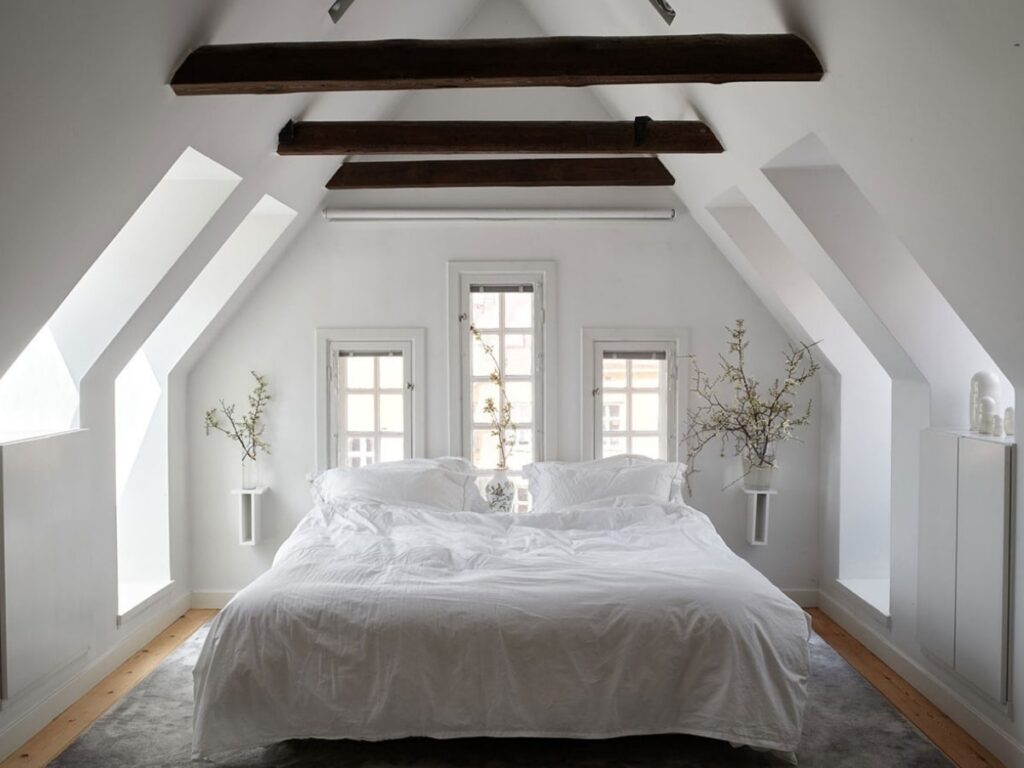 Minimalist bedroom with white decor, wooden beams, and natural light.
