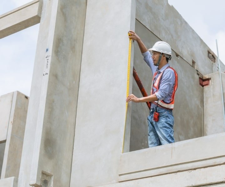 Engineer measuring construction wall height with a tape measure on-site.