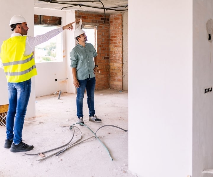 Engineers discussing renovation plans at construction site, wearing helmets.