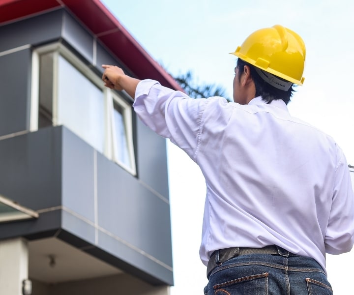 Construction worker pointing at building with safety helmet on site.