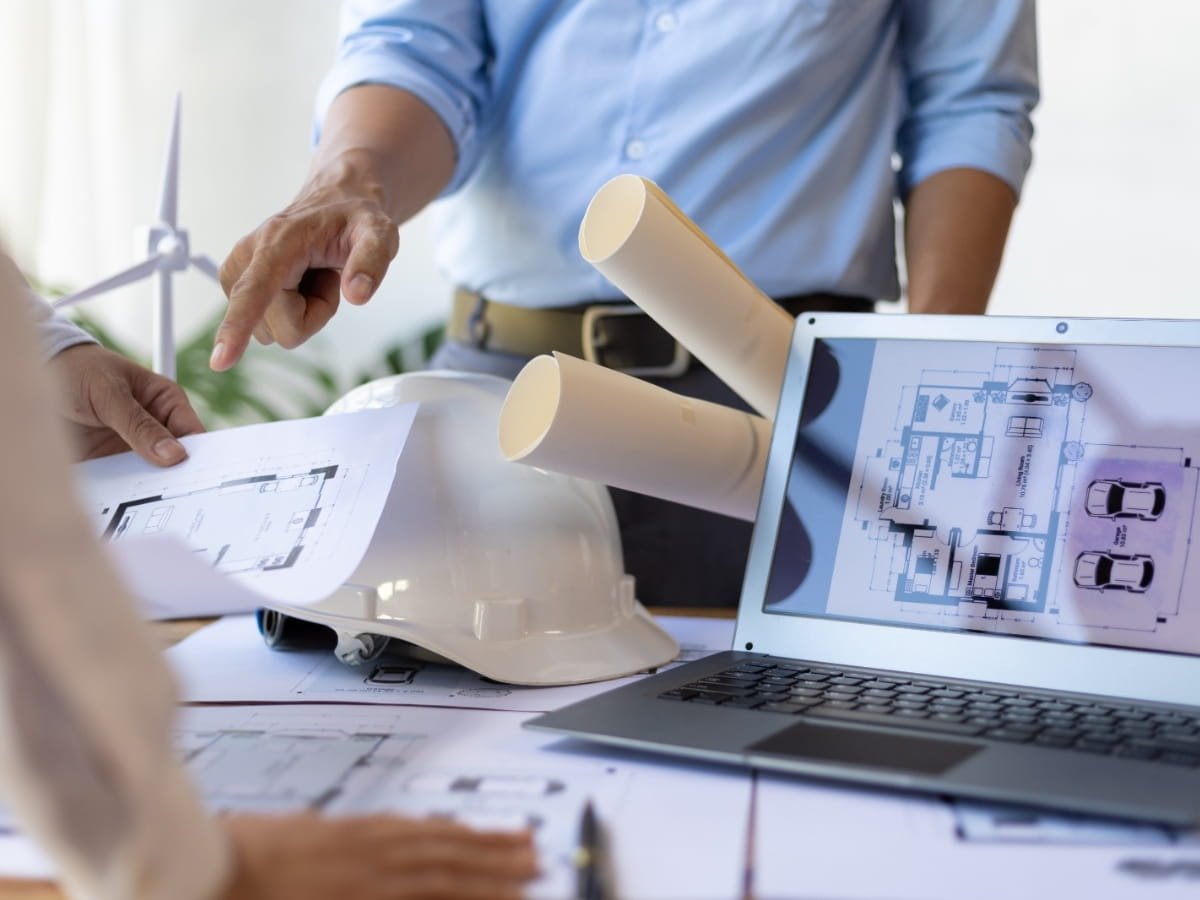 n engineer working table with laptop showcasing architectural autocad design or an auto mechanic's shop with hardcopy plans and an onsite safety helmet in white color.